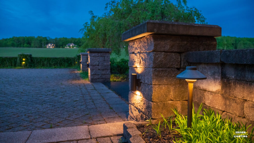 Low voltage landscape lighting highlighting stone entryway pillars and a brick paver walkway